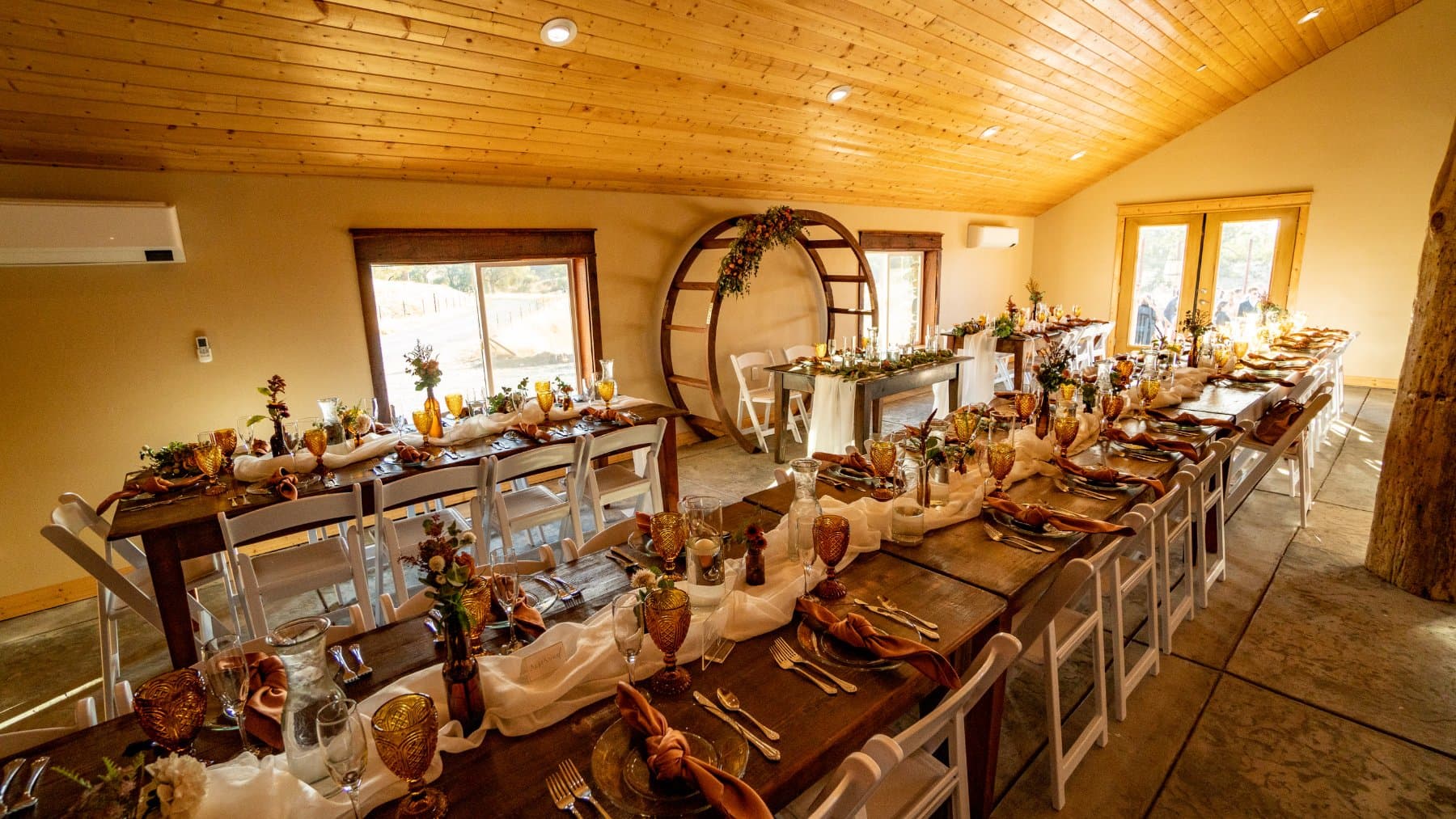 Farm tables running the length of the barn under the pine ceiling, with the circle arch set behind the head table