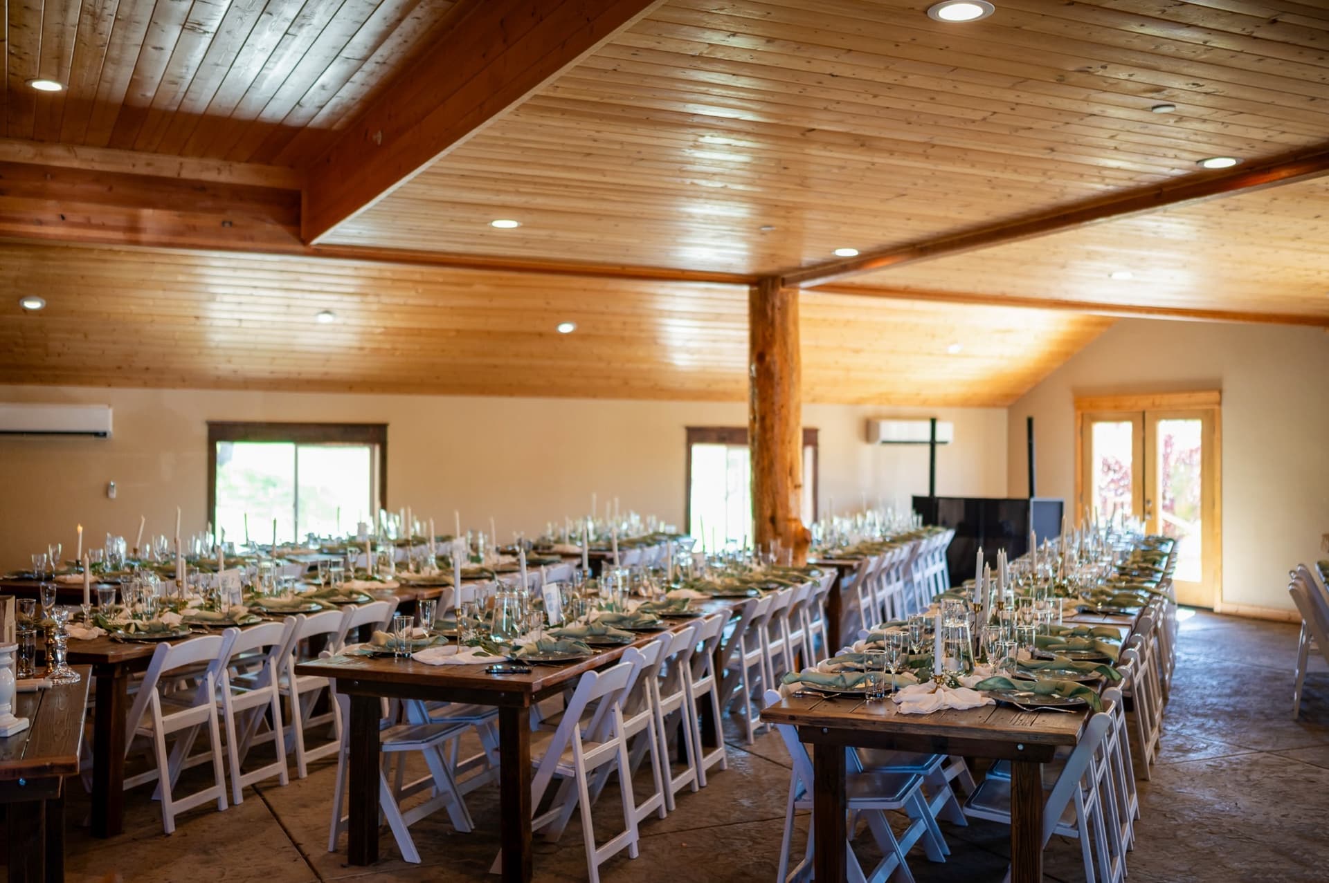 Farm tables dressed with sage napkins and taper candles running the length of the barn wedding venue in the Sierra foothills