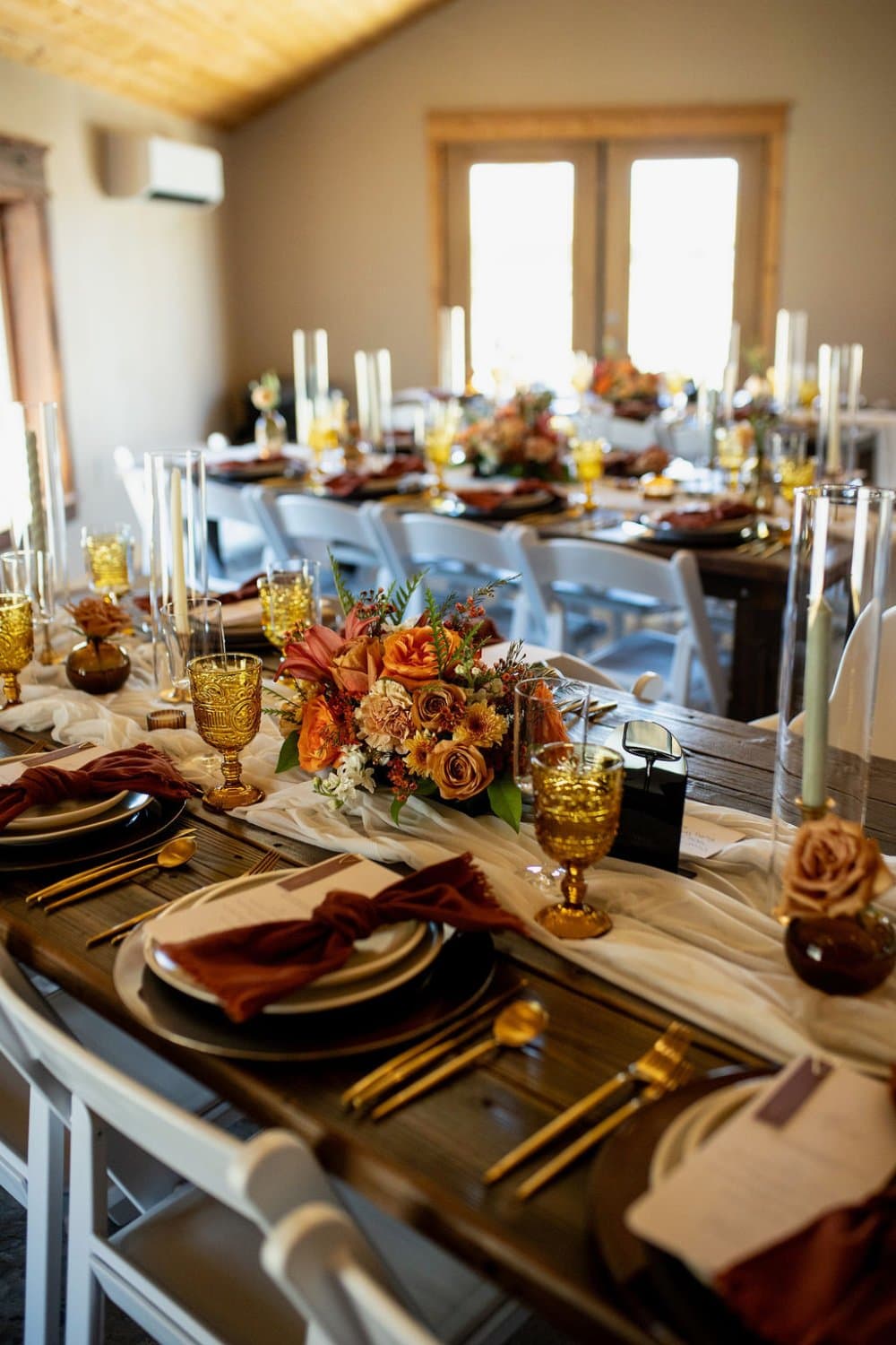 Place setting with a rust velvet napkin, gold flatware and an autumn rose centerpiece on a bare wood farm table