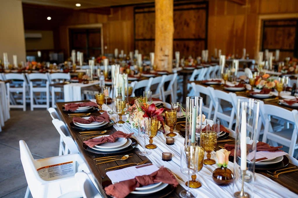 Tables set with rust napkins, black chargers and taper candles filling the barn's main room before guests arrive