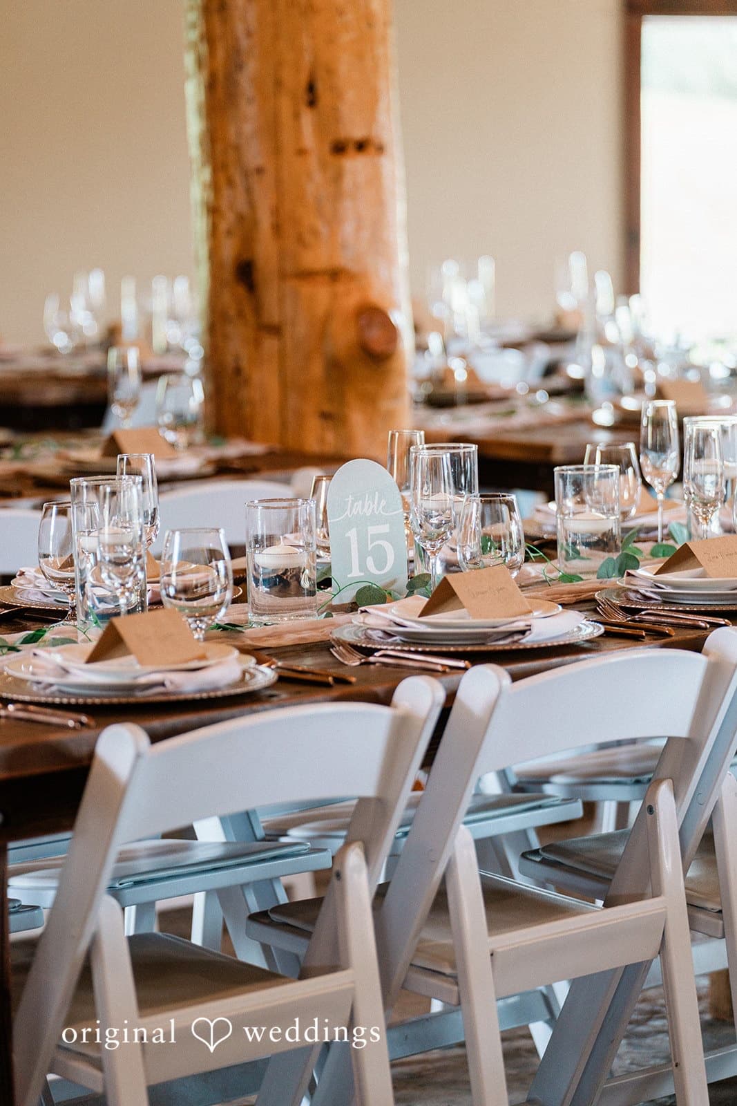 Copper flatware, kraft place cards and a hand-lettered table number down a farm table by the barn's timber post