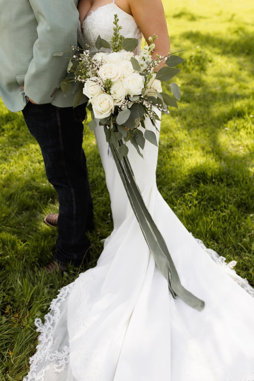 Bride's white rose and eucalyptus bouquet with long sage silk ribbons trailing over her train