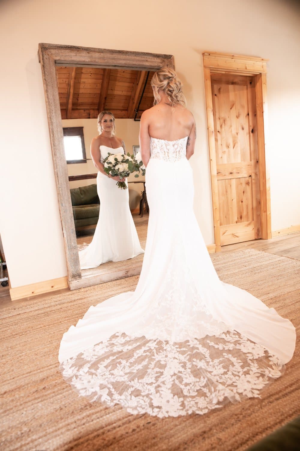 Bride at the antique full-length mirror in the upstairs bridal suite with her lace cathedral train spread across the jute rug