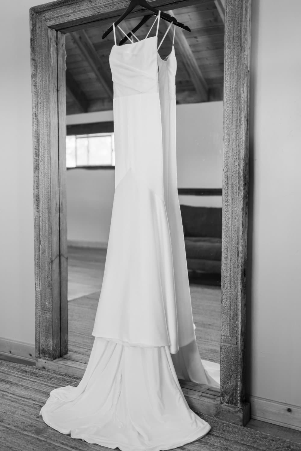 Black and white photograph of a wedding gown hanging on the reclaimed-wood mirror in the bridal suite