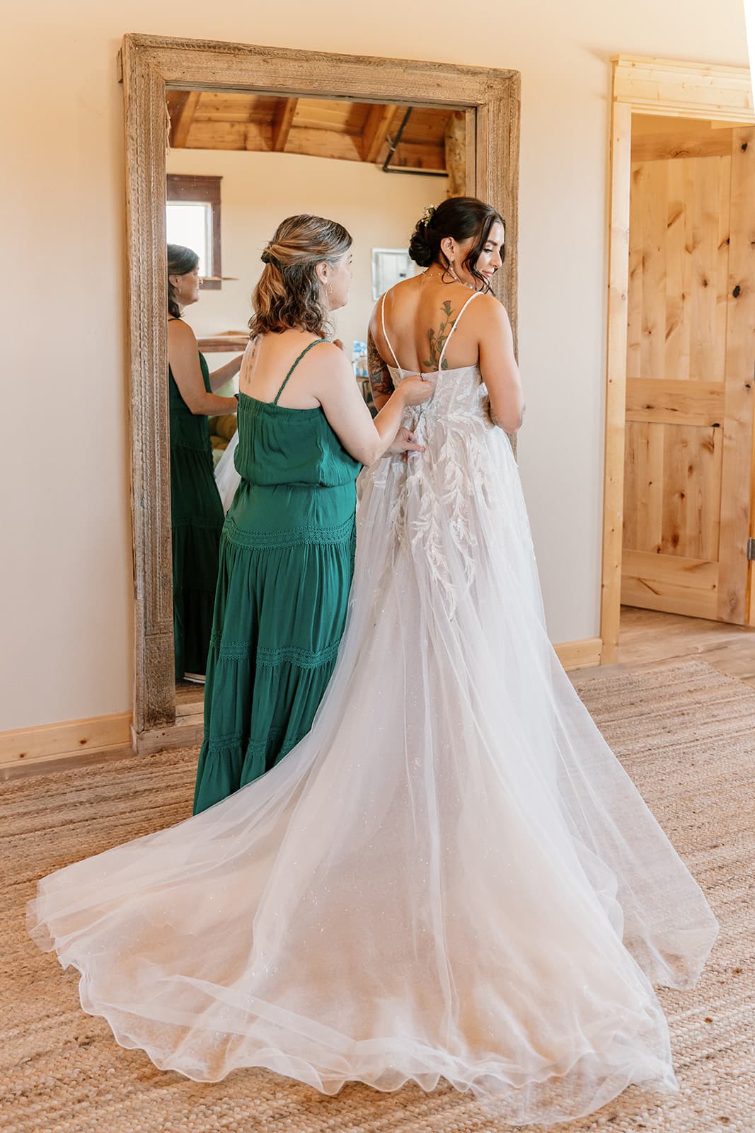 Mother of the bride fastens the last buttons of the gown at the bridal suite's reclaimed-wood mirror