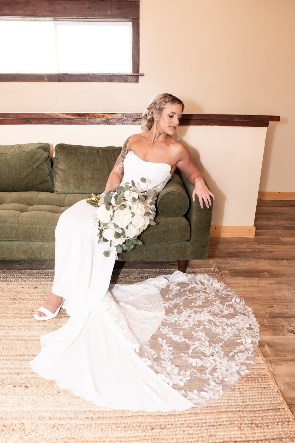 Bride seated on the green velvet sofa in the bridal suite with her train and bouquet across the cushion