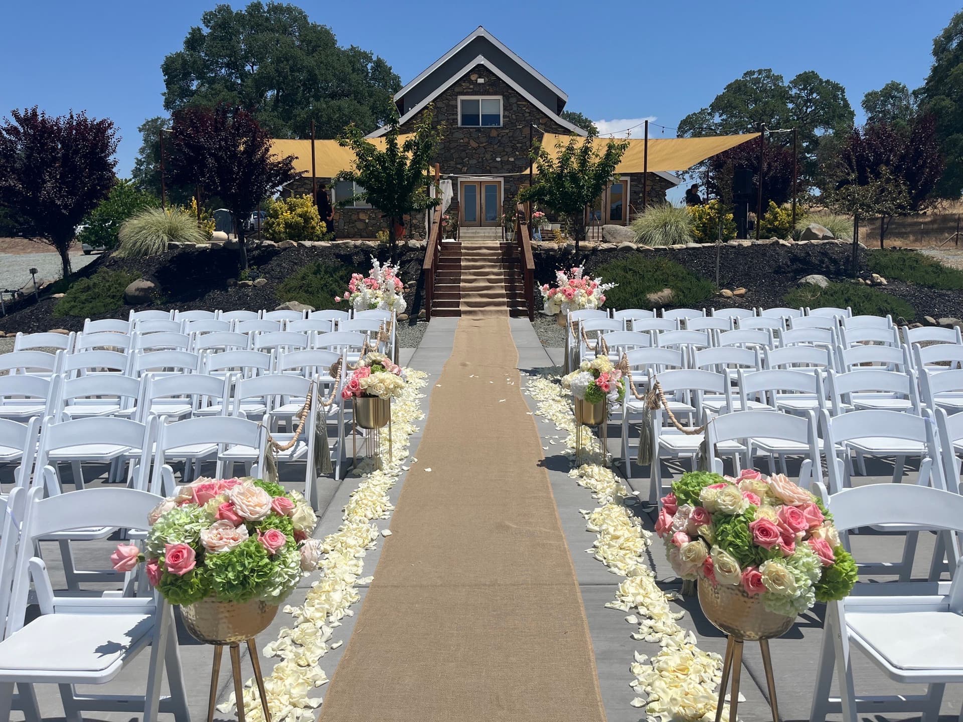 Burlap aisle runner scattered with rose petals leading to the stone barn steps at a rustic barn wedding, white chairs either side