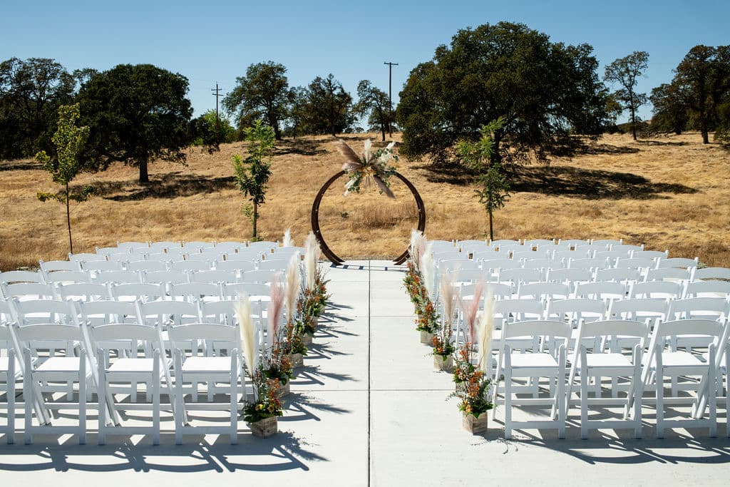 Circle arch dressed with pampas grass above the dry golden hillside at a late-summer country wedding, pampas and rust florals lining the aisle
