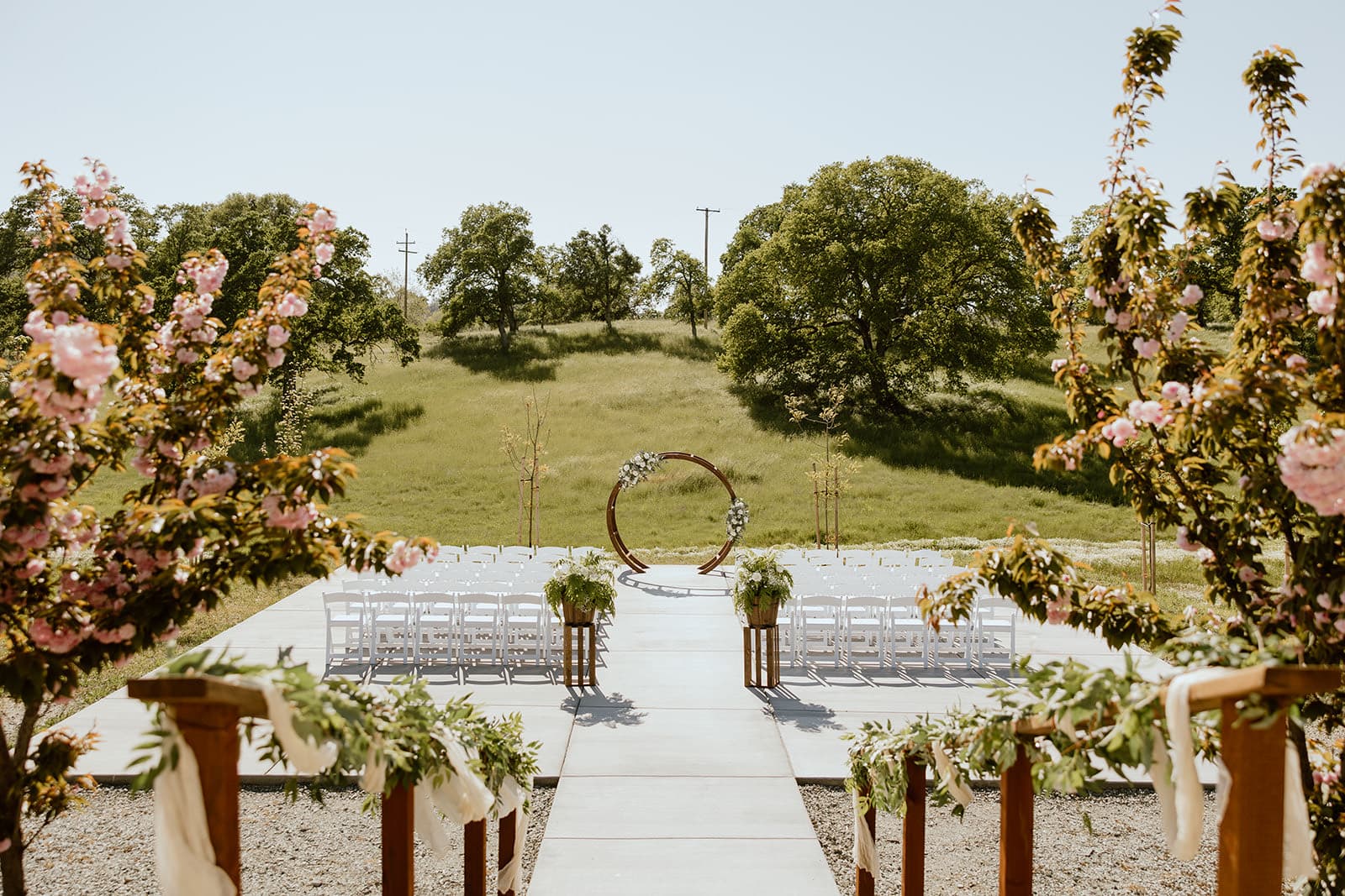 The circle arch on the green spring hillside framed by flowering pink blossom trees at a Gold Country wedding