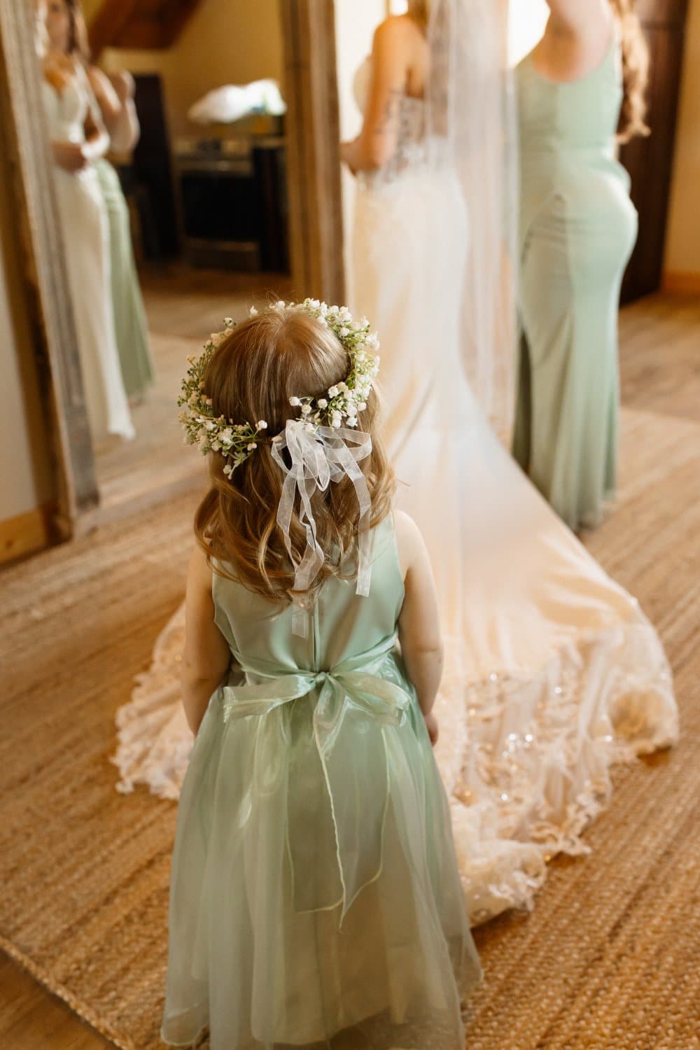 Flower girl in a sage tulle dress and baby's breath crown watches the bride get ready in the suite