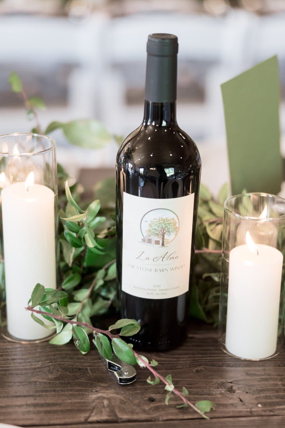 Bottle of La Alma red wine from The Stone Barn Winery between pillar candles and greenery on a reception table