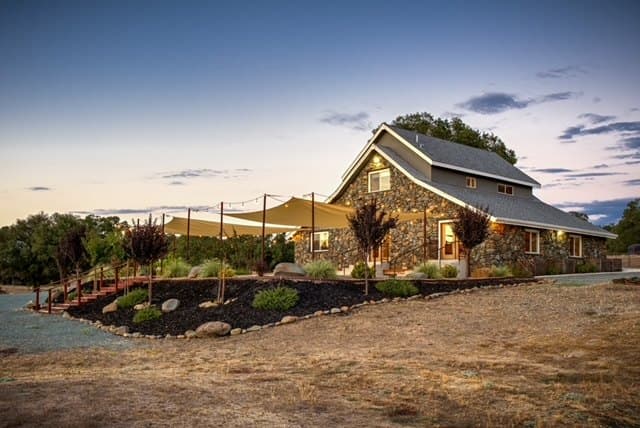 Side view of the barn at dusk with shade sails stretched over the patio and oaks along the ridge