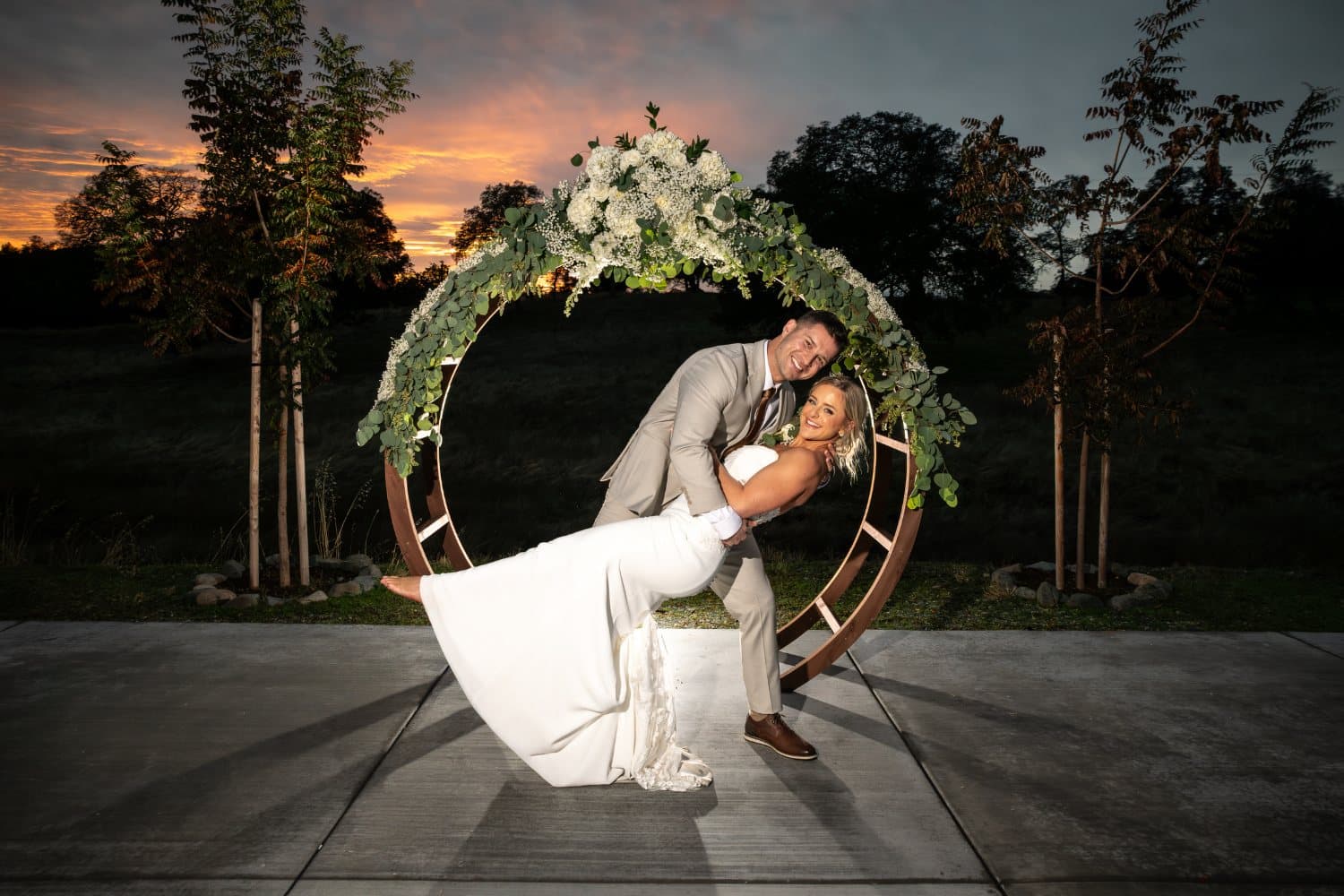 Groom dips the bride for a kiss beneath the floral circle arch after sunset at The Stone Barn Winery