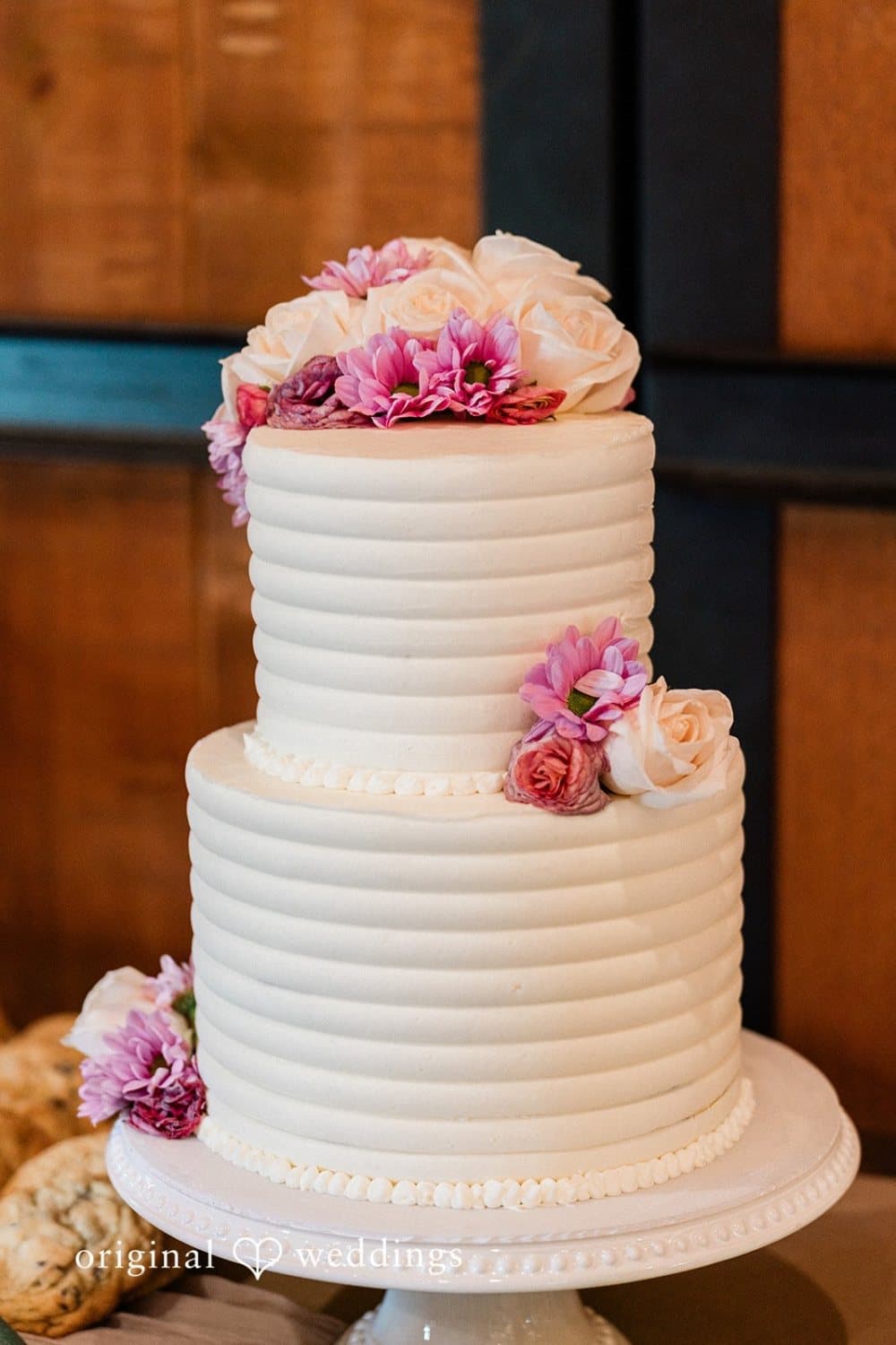 Two-tier buttercream wedding cake trimmed with pink dahlias and cream roses inside the stone barn
