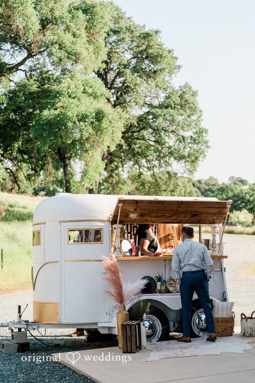 Guest ordering a drink at the restored vintage horse-trailer bar parked under the oaks
