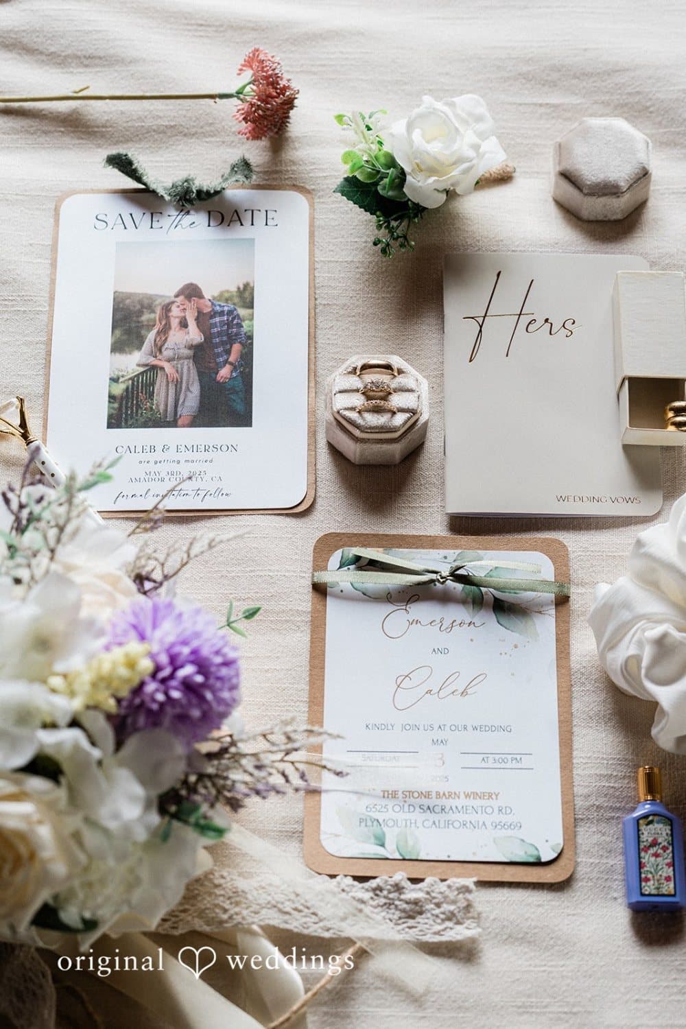 Flat lay of a save-the-date, invitation, vow books and rings on linen with white and lilac florals