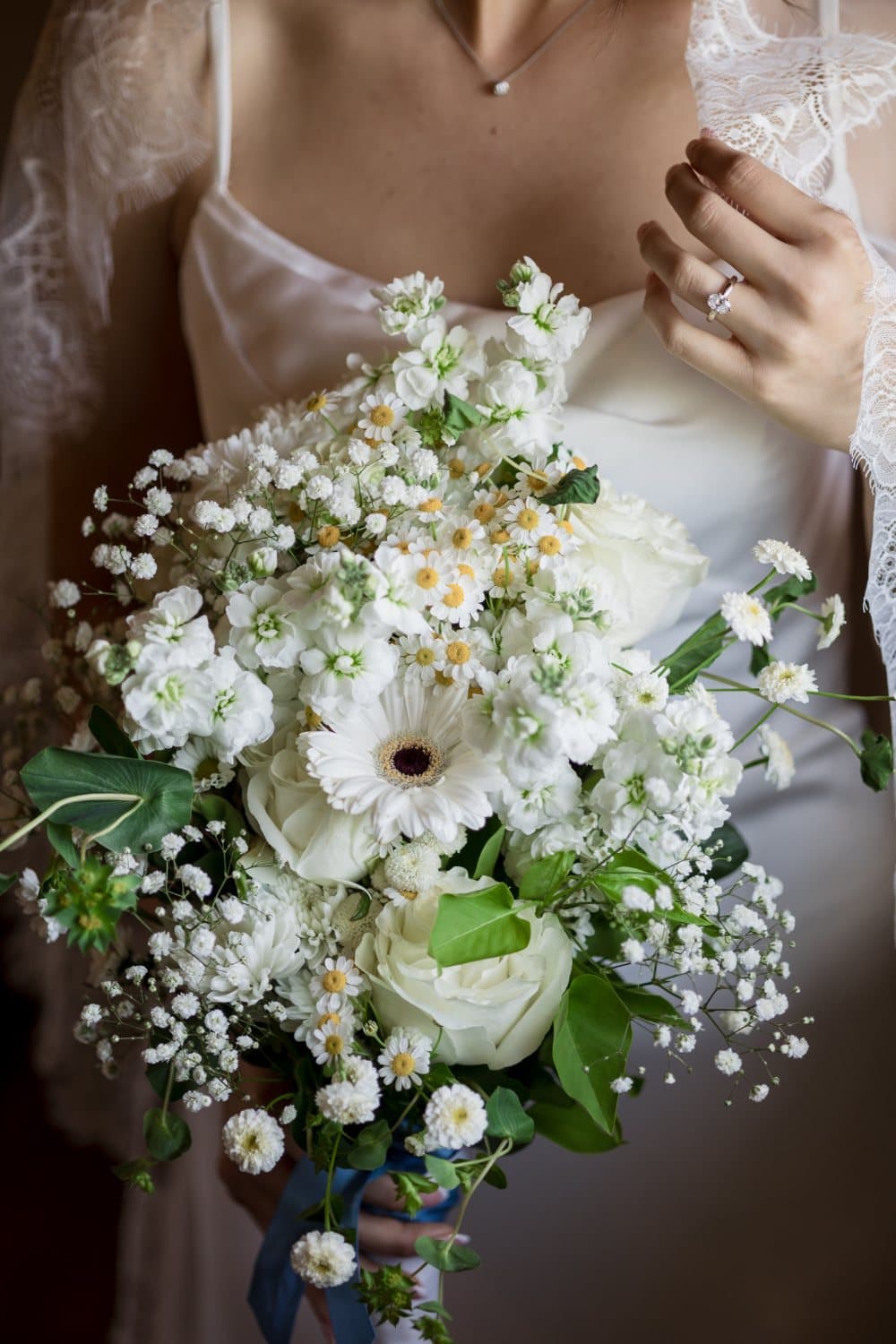 Close-up of a white garden bouquet of roses, chamomile and baby's breath held by the bride
