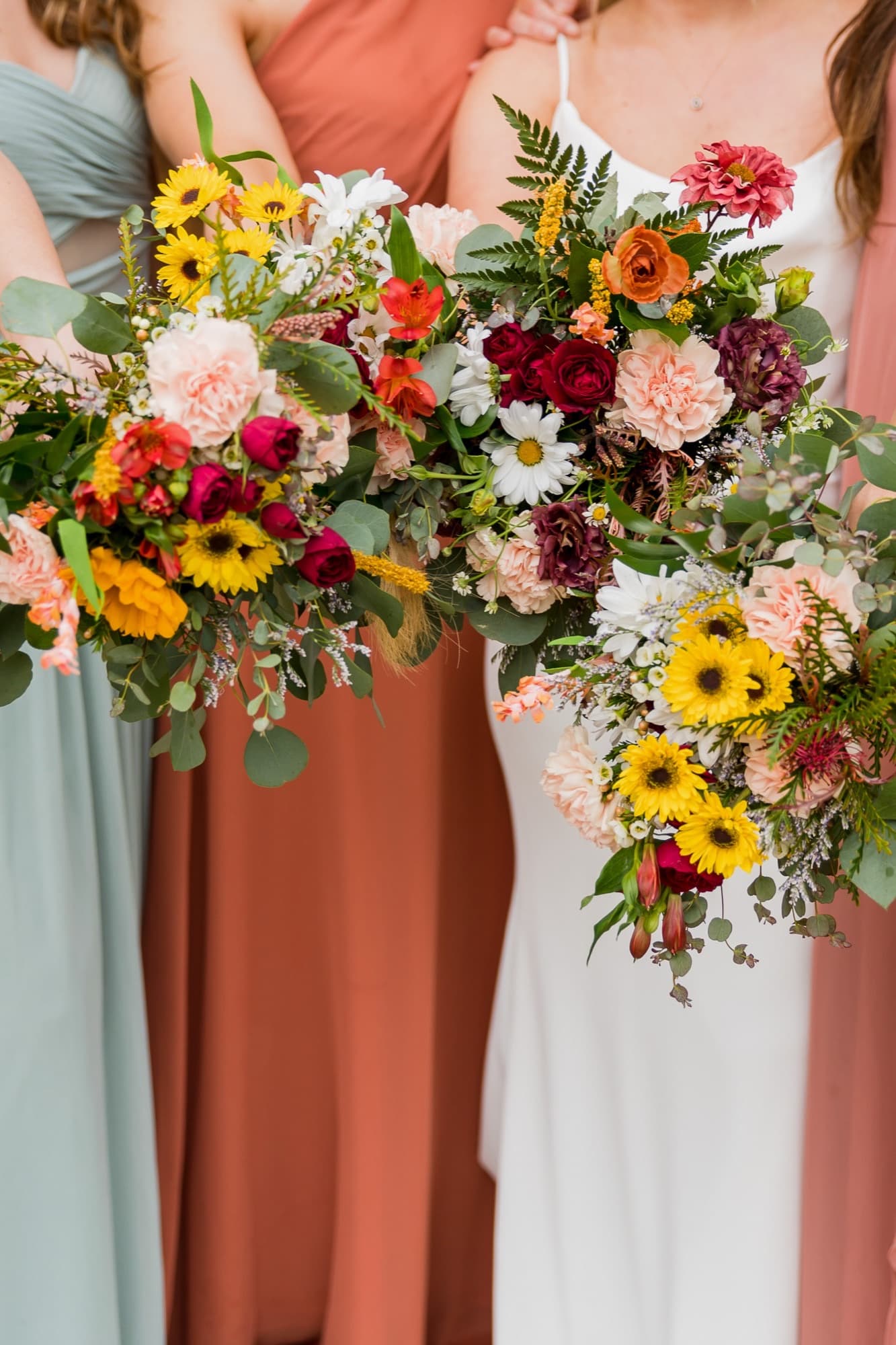 Three wildflower bouquets of daisies, roses and carnations held by the bride and her bridesmaids at a country wedding
